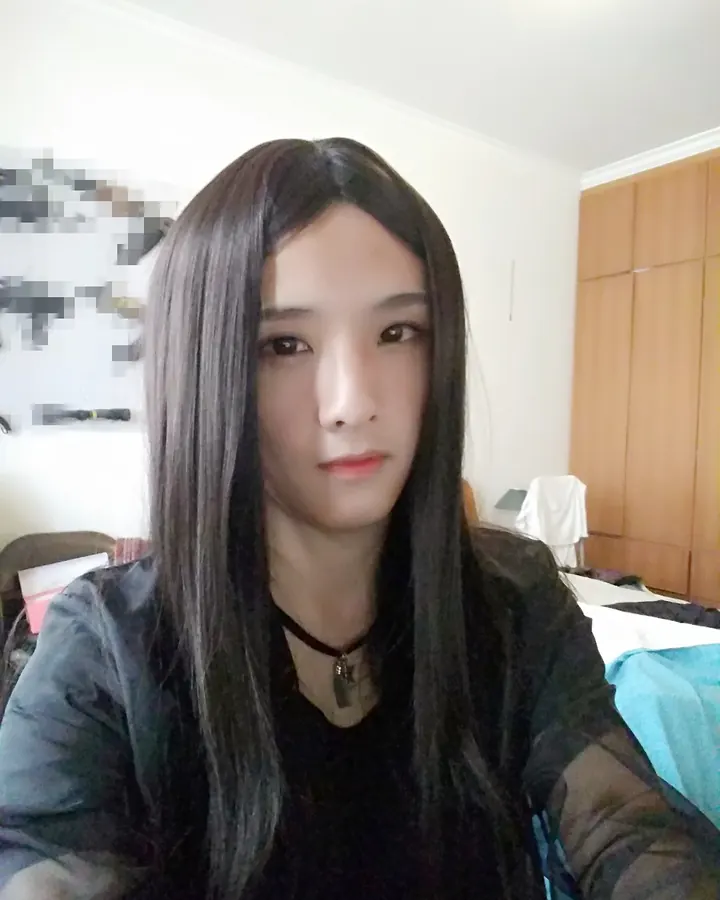 Femme trans aux cheveux bruns, vêtue d’un haut noir et d’un short noir, prenant un selfie devant un miroir, une main sur la hanche.