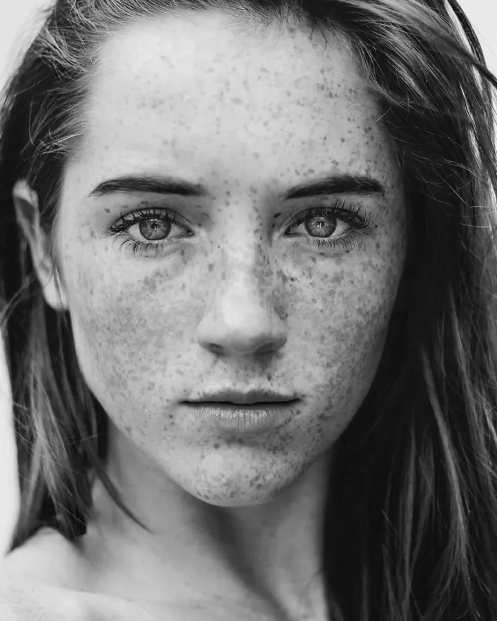 Portrait en noir et blanc d'une femme trans aux yeux gris et aux taches de rousseur, regardant directement l'objectif.