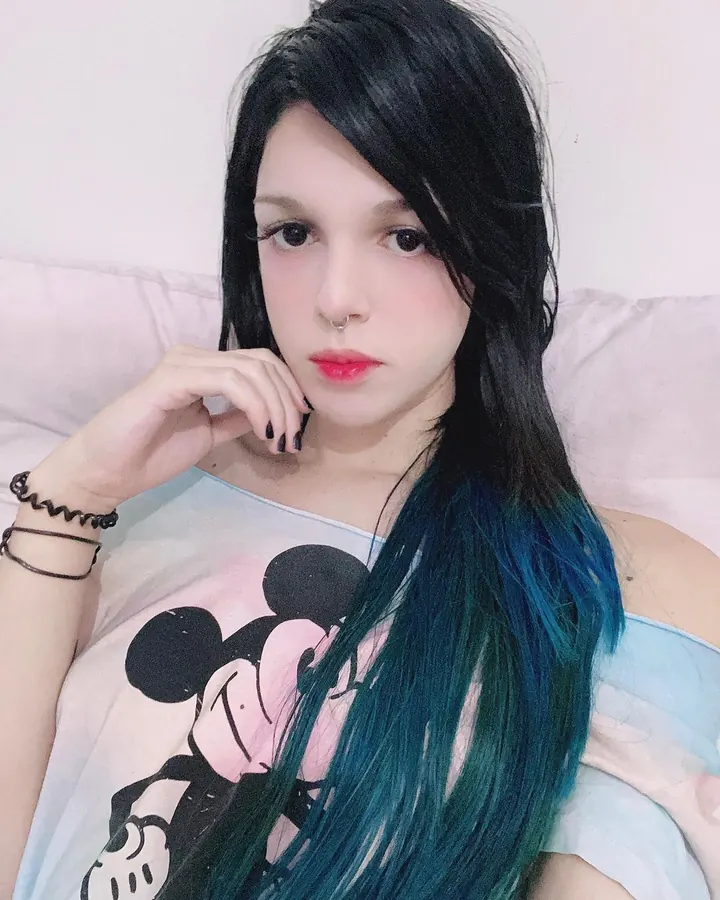 Femme trans en tenue de latex noir, regardant son reflet dans un miroir.