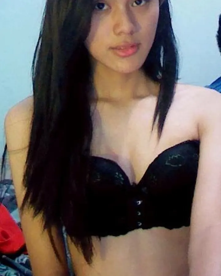 Femme trans asiatique aux cheveux bruns-noirs, portant un haut noir à lacets, regardant directement l'appareil photo.