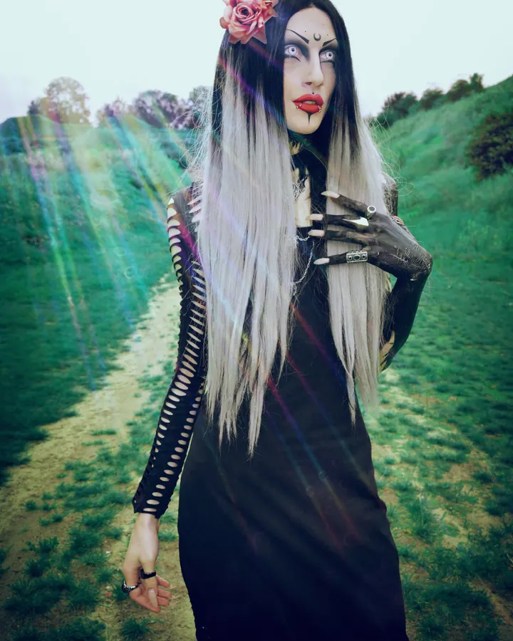 Femme trans latino aux cheveux blancs, portant un haut noir, assise sur un canapé rouge, regardant l'appareil photo.