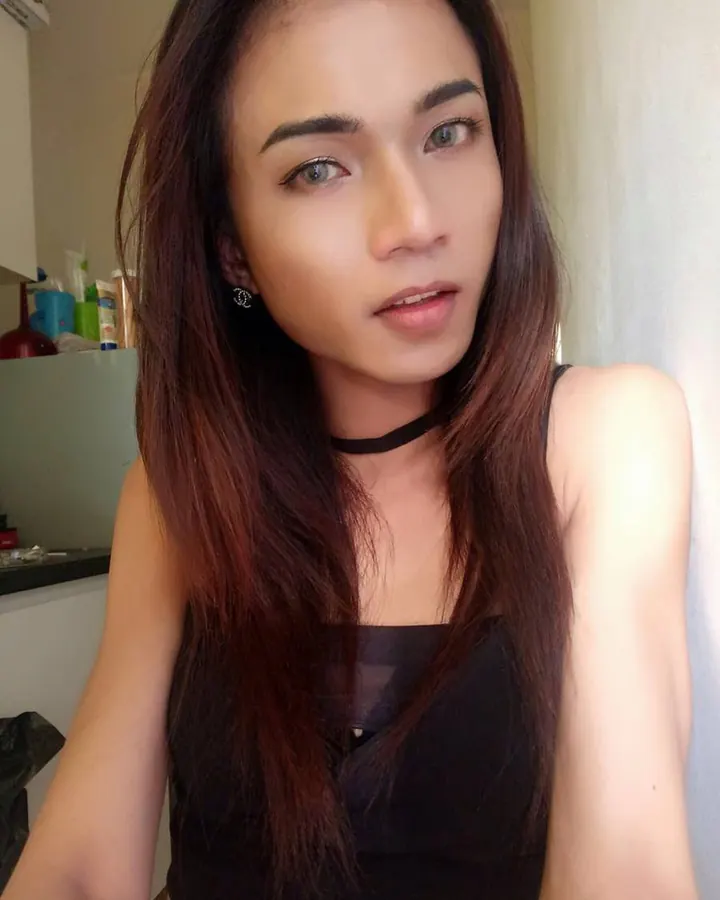 Femme trans en haut blanc, assise sur une chaise, regard direct, cheveux longs, ambiance intime