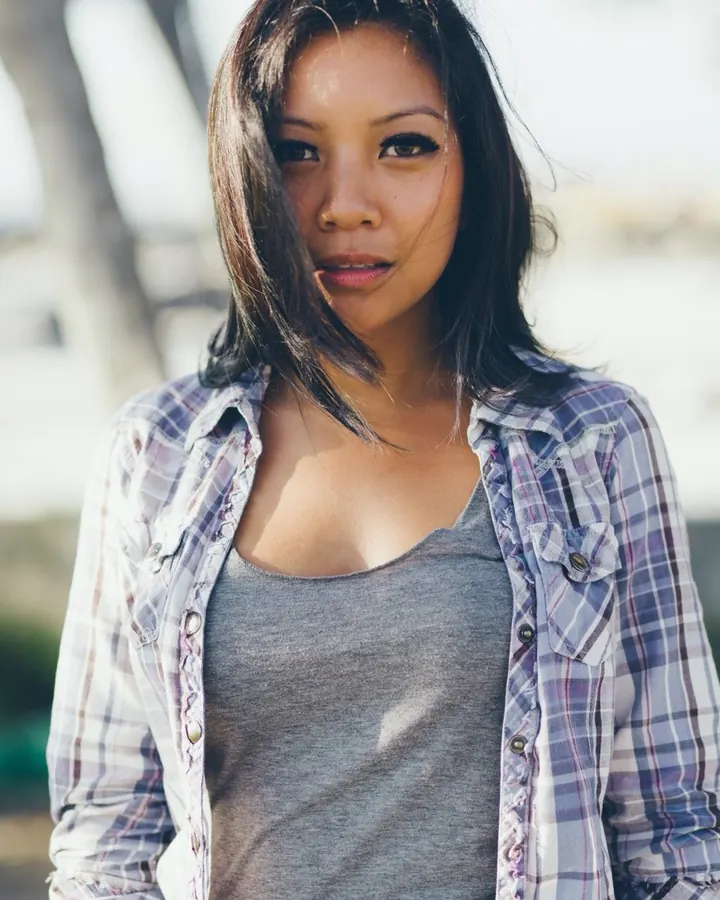 Femme trans latino aux cheveux bruns-noirs et yeux marrons, en lingerie blanche, allongée sur un lit, avec un fond flou.