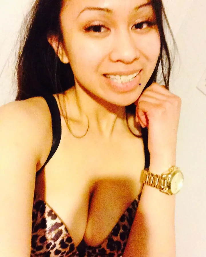 Jeune femme trans aux cheveux bruns foncés en soutien-gorge léopard, souriant à la caméra avec une montre dorée au poignet.