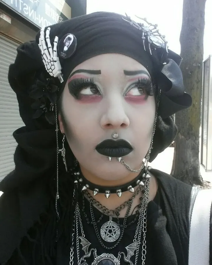 Jeune femme trans aux cheveux bruns, portant un haut noir, les mains sur les hanches.