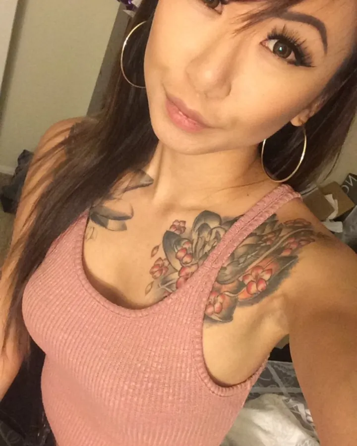 Femme trans aux cheveux bruns, prenant un selfie, portant un haut noir.