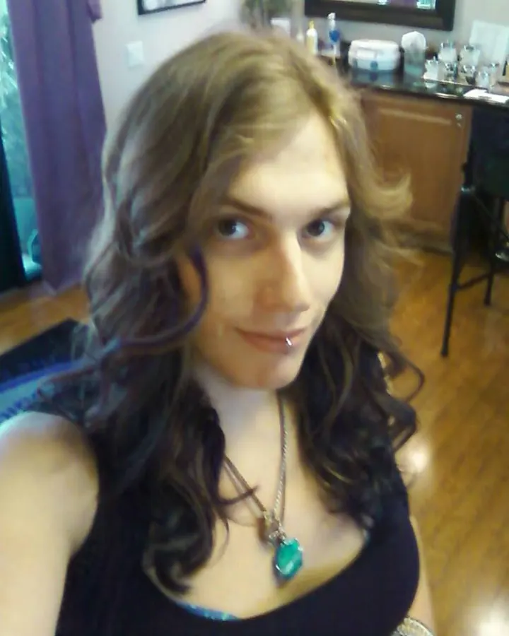 Femme trans aux cheveux blonds, portant un haut noir en dentelle, les mains dans les cheveux.