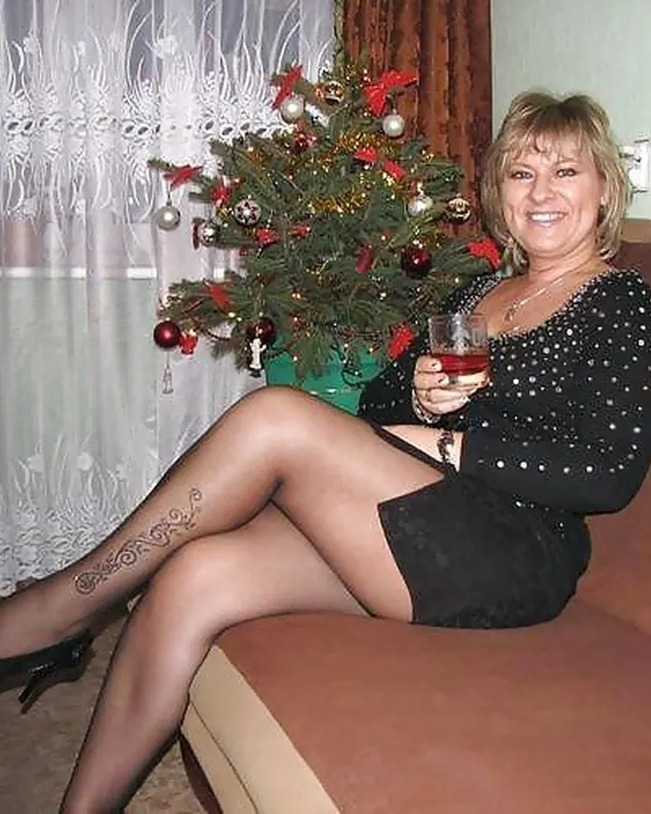 Femme trans aux cheveux blonds, portant un haut noir, posant avec un regard intense et un sourire discret.